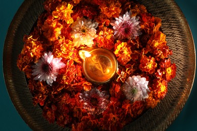 Photo of Diwali celebration. Diya lamp and beautiful flowers on turquoise background, top view