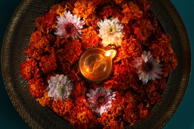 Photo of Diwali celebration. Diya lamp and beautiful flowers on turquoise background, top view