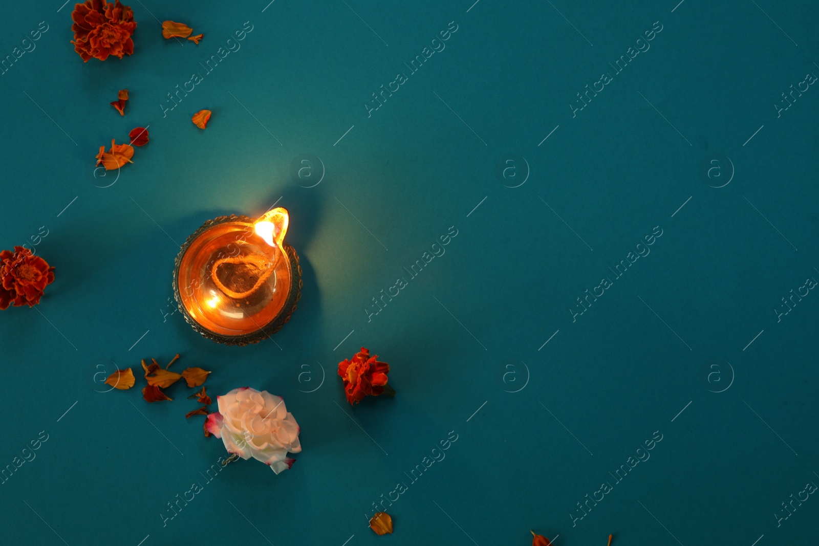 Photo of Diwali celebration. Diya lamp and beautiful flowers on turquoise background, top view. Space for text