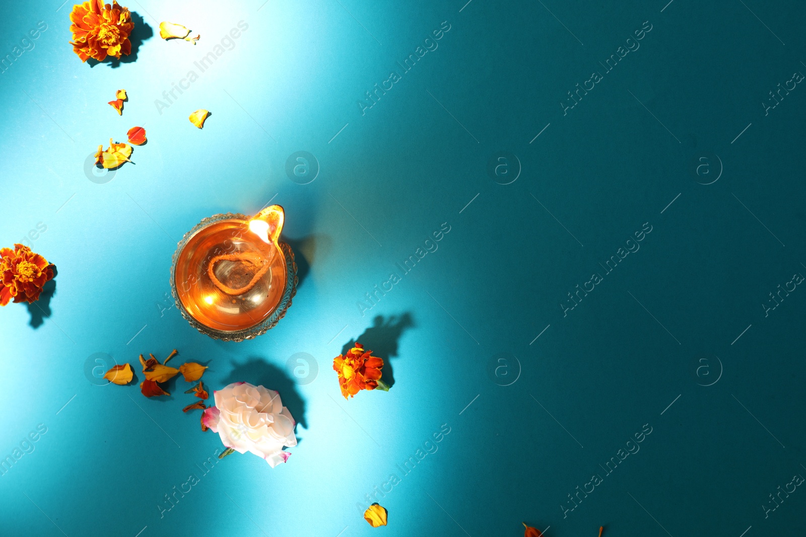 Photo of Diwali celebration. Diya lamp and beautiful flowers on turquoise background, top view. Space for text