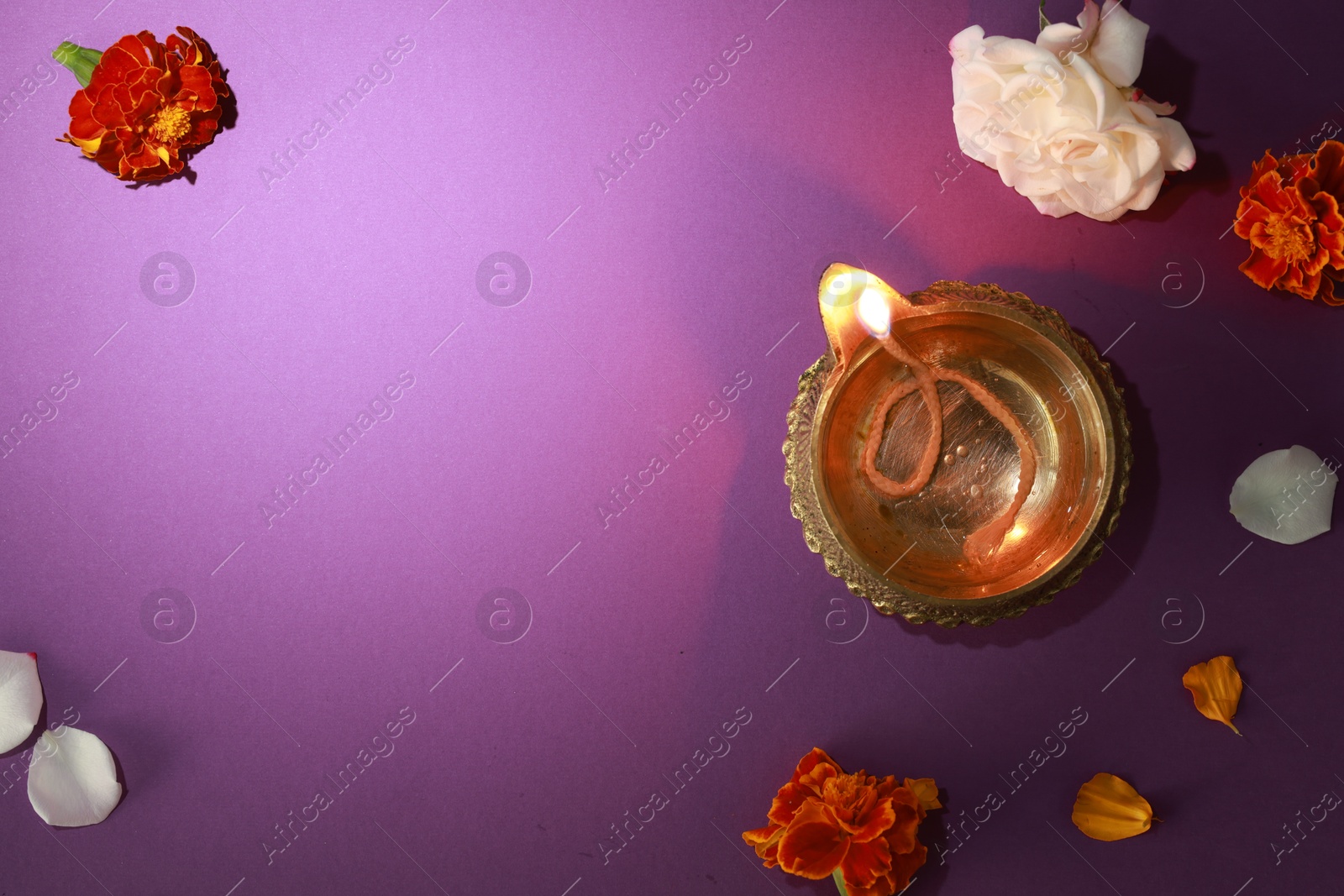 Photo of Diwali celebration. Diya lamp and beautiful flowers on purple background, top view. Space for text