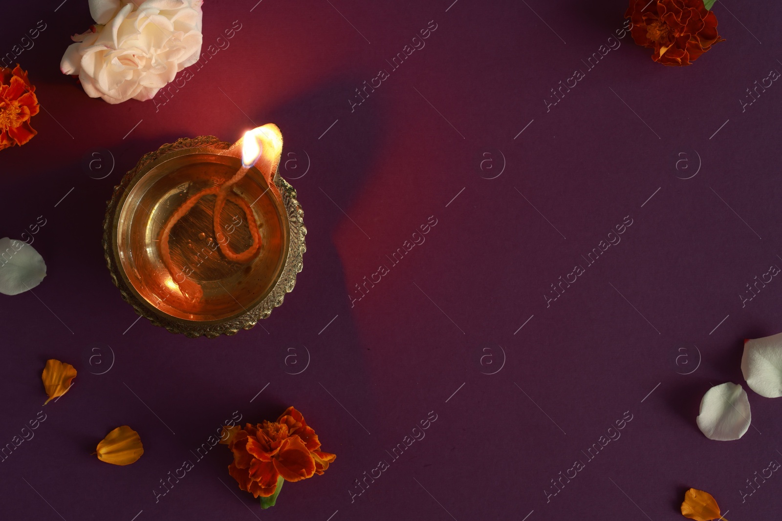 Photo of Diwali celebration. Diya lamp and beautiful flowers on purple background, top view. Space for text