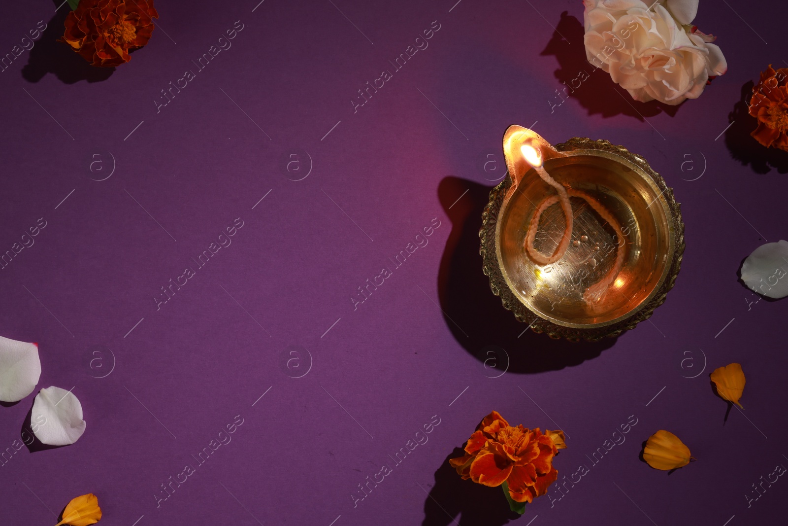 Photo of Diwali celebration. Diya lamp and beautiful flowers on purple background, top view. Space for text