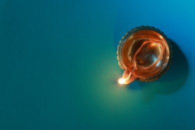 Photo of Diwali celebration. Diya lamp on teal background, top view. Space for text