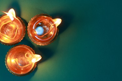 Diwali celebration. Diya lamps on teal background, flat lay. Space for text