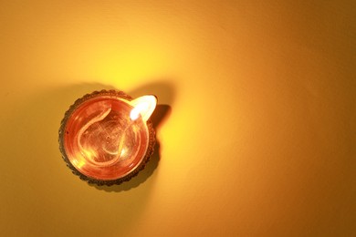 Diwali celebration. Diya lamp on orange background, top view. Space for text