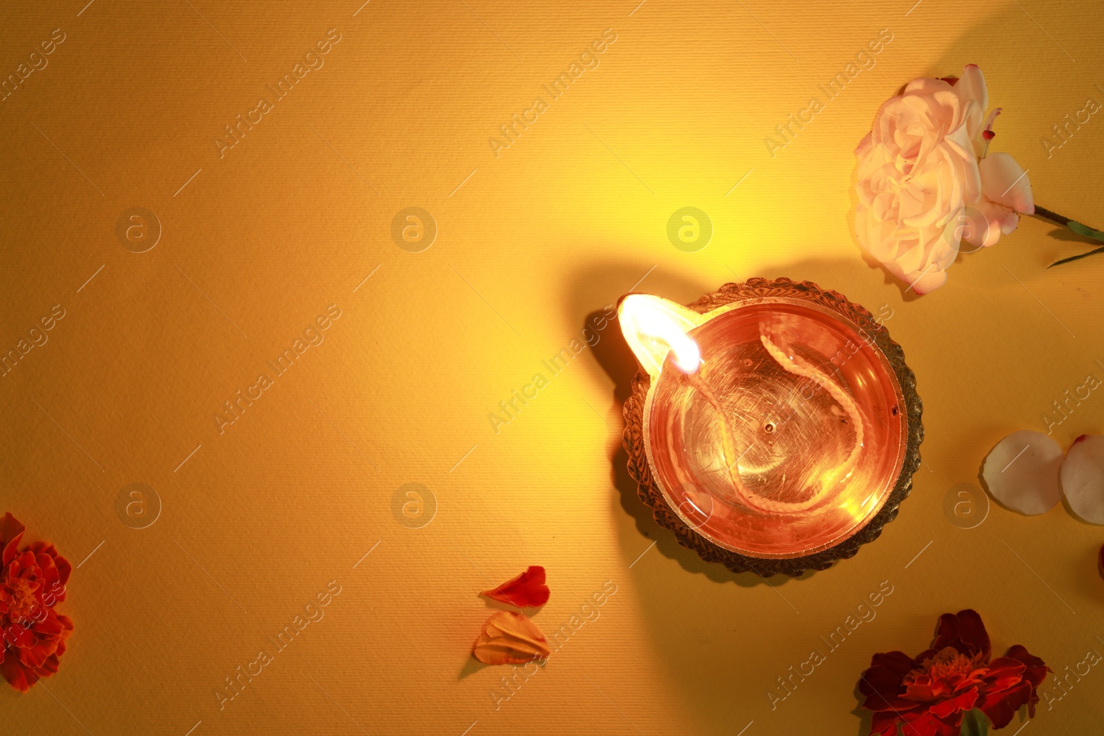 Photo of Diwali celebration. Diya lamp and beautiful flowers on orange background, top view. Space for text