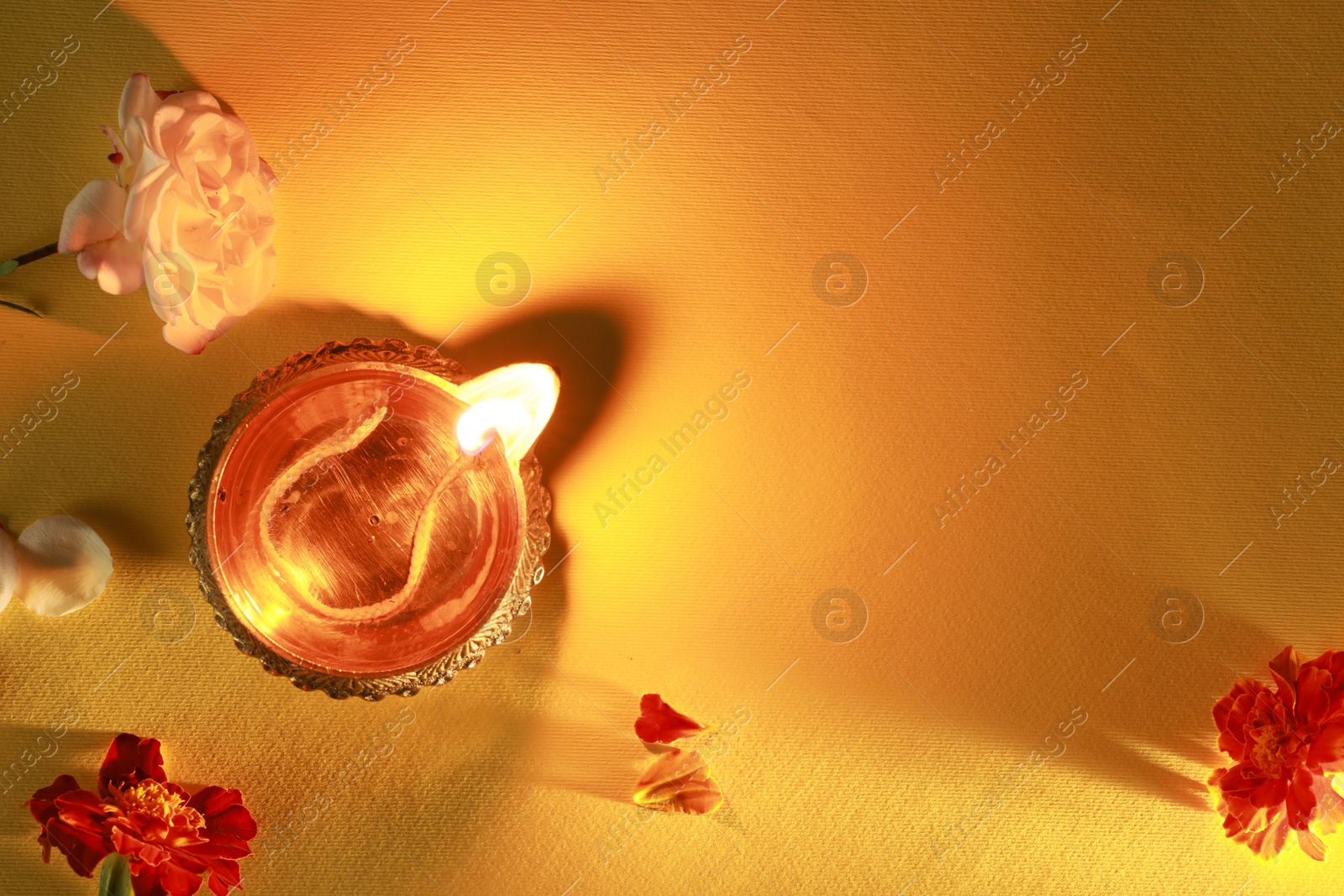 Photo of Diwali celebration. Diya lamp and beautiful flowers on orange background, top view. Space for text