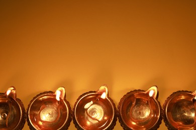 Photo of Diwali celebration. Diya lamps on orange background, flat lay. Space for text