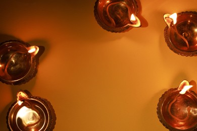 Photo of Diwali celebration. Diya lamps on orange background, flat lay. Space for text