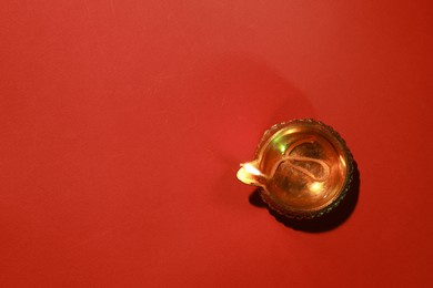 Photo of Diwali celebration. Diya lamp on red background, top view. Space for text