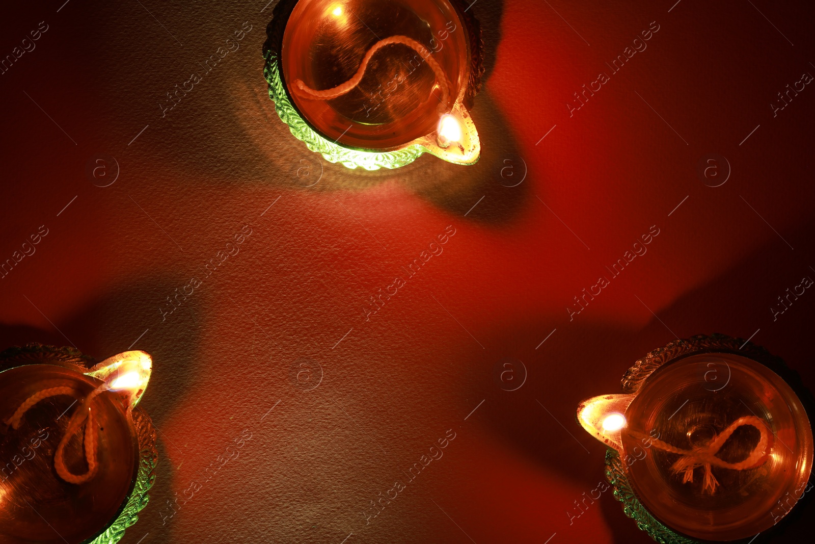 Photo of Diwali celebration. Diya lamps on red background, flat lay. Space for text