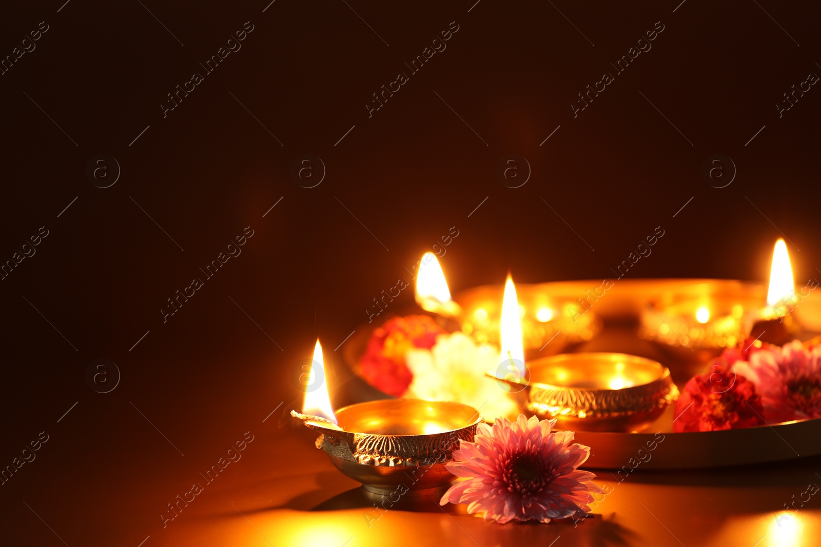 Photo of Diwali celebration. Diya lamps and beautiful flowers on color background, closeup. Space for text