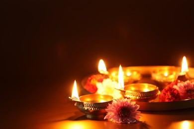 Photo of Diwali celebration. Diya lamps and beautiful flowers on color background, closeup. Space for text