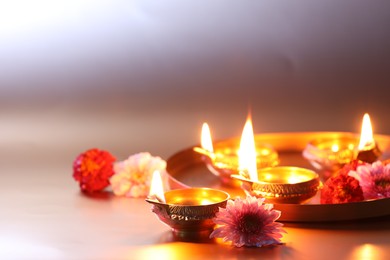 Photo of Diwali celebration. Diya lamps and beautiful flowers on light background, closeup. Space for text