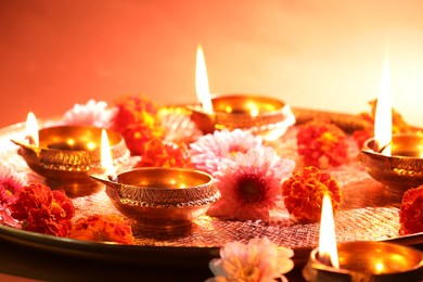 Diwali celebration. Diya lamps and beautiful flowers on color background, closeup