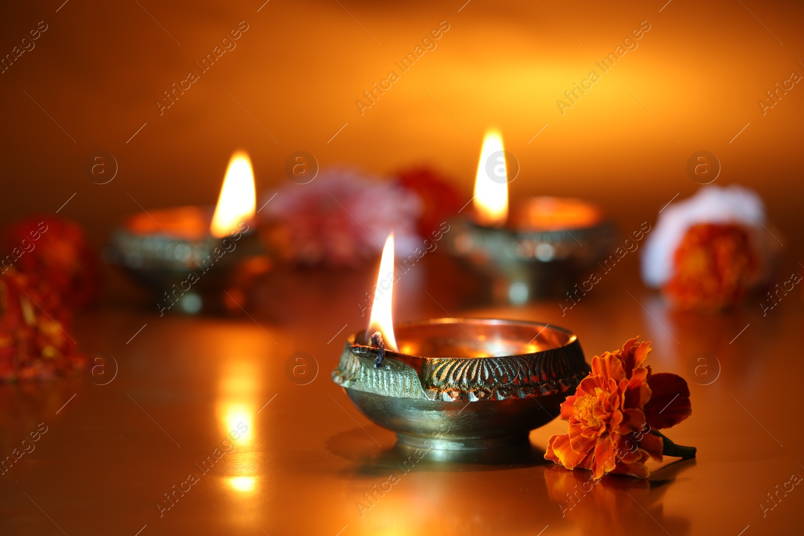 Photo of Diwali celebration. Diya lamps and beautiful flowers on golden background, closeup