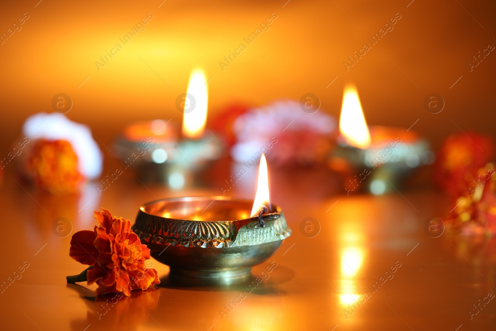 Photo of Diwali celebration. Diya lamps and beautiful flowers on golden background, closeup