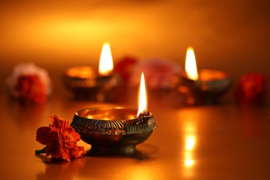 Photo of Diwali celebration. Diya lamps and beautiful flowers on golden background, closeup