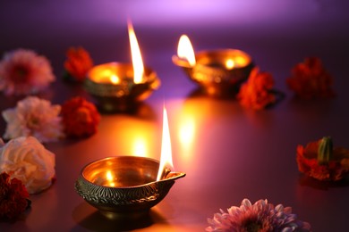 Photo of Diwali celebration. Diya lamps and beautiful flowers on color background, closeup