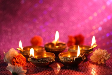 Diwali celebration. Diya lamps and beautiful flowers on color background, closeup