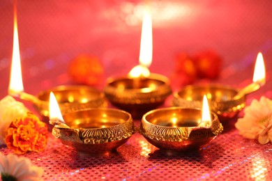 Diwali celebration. Diya lamps and beautiful flowers on color background, closeup