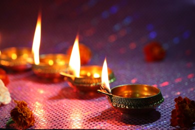 Diwali celebration. Diya lamps and beautiful flowers on color background, closeup