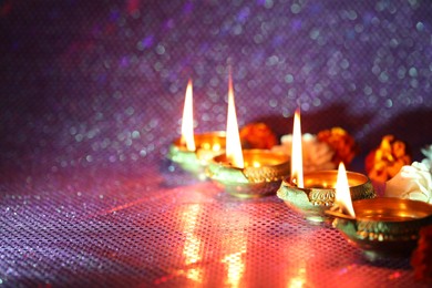 Photo of Diwali celebration. Diya lamps and beautiful flowers on color background, closeup. Space for text