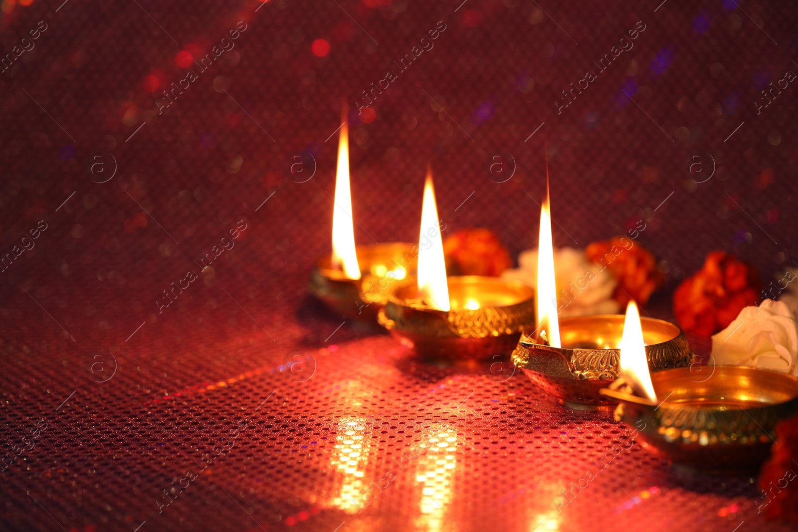 Photo of Diwali celebration. Diya lamps and beautiful flowers on color background, closeup. Space for text