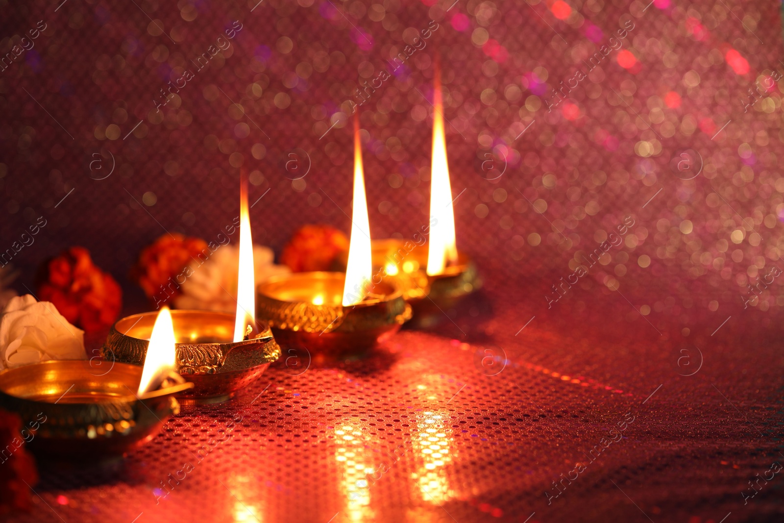 Photo of Diwali celebration. Diya lamps and beautiful flowers on color background, closeup. Space for text