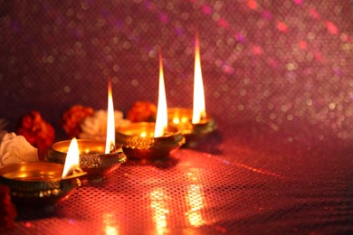 Photo of Diwali celebration. Diya lamps and beautiful flowers on color background, closeup. Space for text