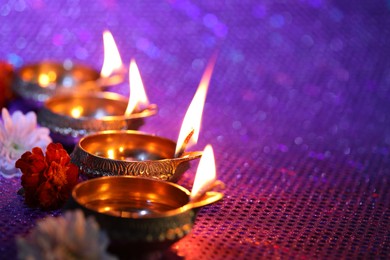 Photo of Diwali celebration. Diya lamps and beautiful flowers on color background, closeup. Space for text