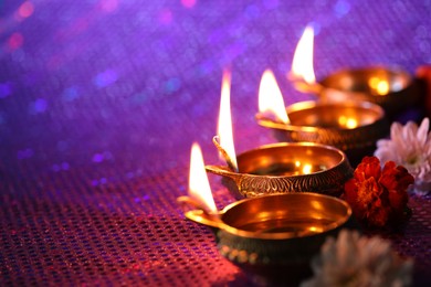 Photo of Diwali celebration. Diya lamps and beautiful flowers on color background, closeup. Space for text