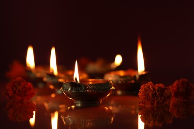 Photo of Diwali celebration. Diya lamps and beautiful flowers on dark background, closeup