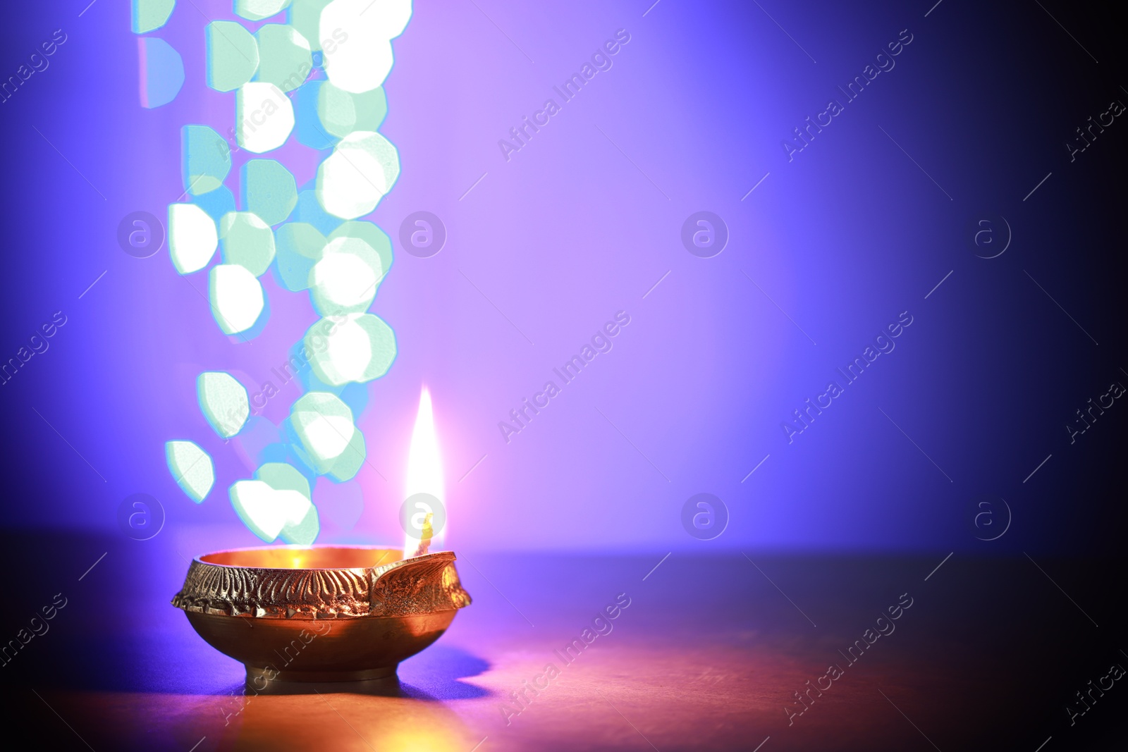 Photo of Diwali celebration. Diya lamp on dark table against blurred lights. Space for text