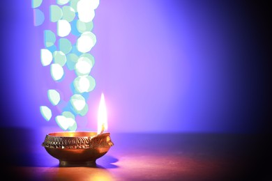 Diwali celebration. Diya lamp on dark table against blurred lights. Space for text