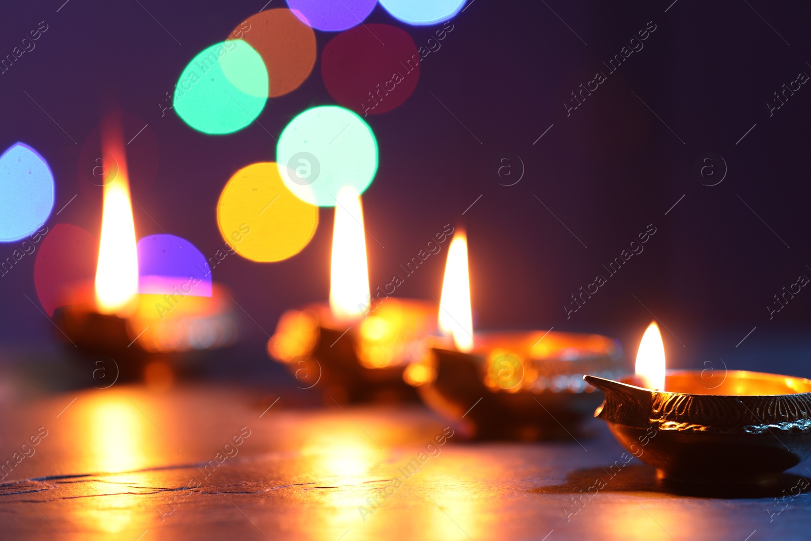 Photo of Diwali celebration. Diya lamps on dark table against blurred lights, closeup