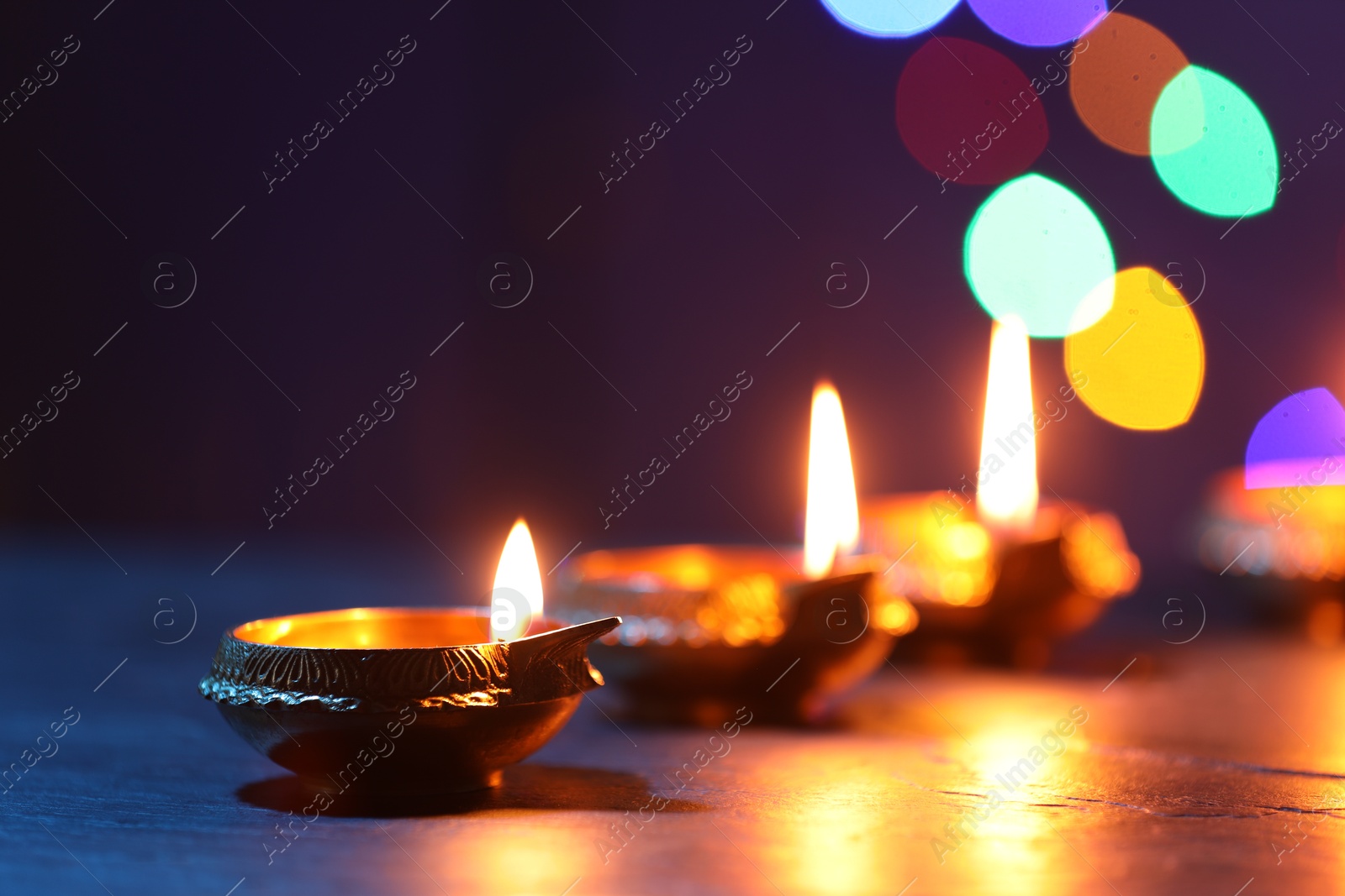 Photo of Diwali celebration. Diya lamps on dark table against blurred lights, closeup