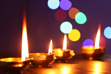 Diwali celebration. Diya lamps on dark table against blurred lights, closeup