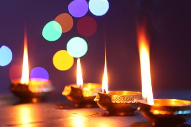 Photo of Diwali celebration. Diya lamps on dark table against blurred lights, closeup