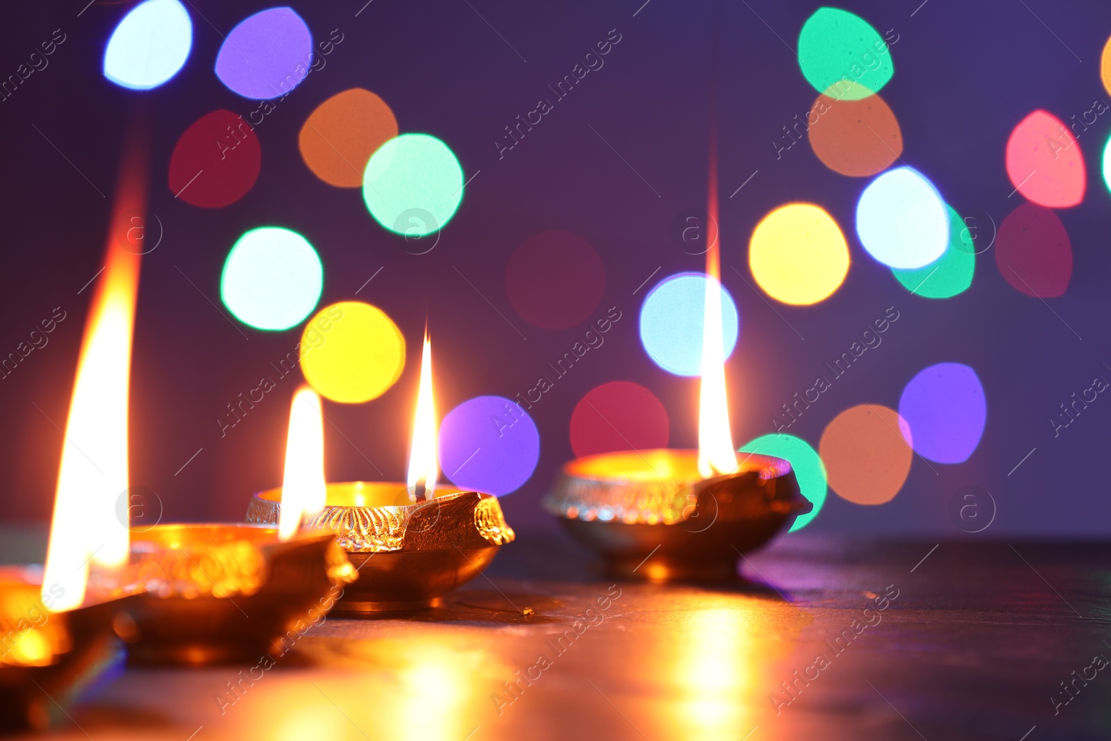 Photo of Diwali celebration. Diya lamps on dark table against blurred lights, closeup