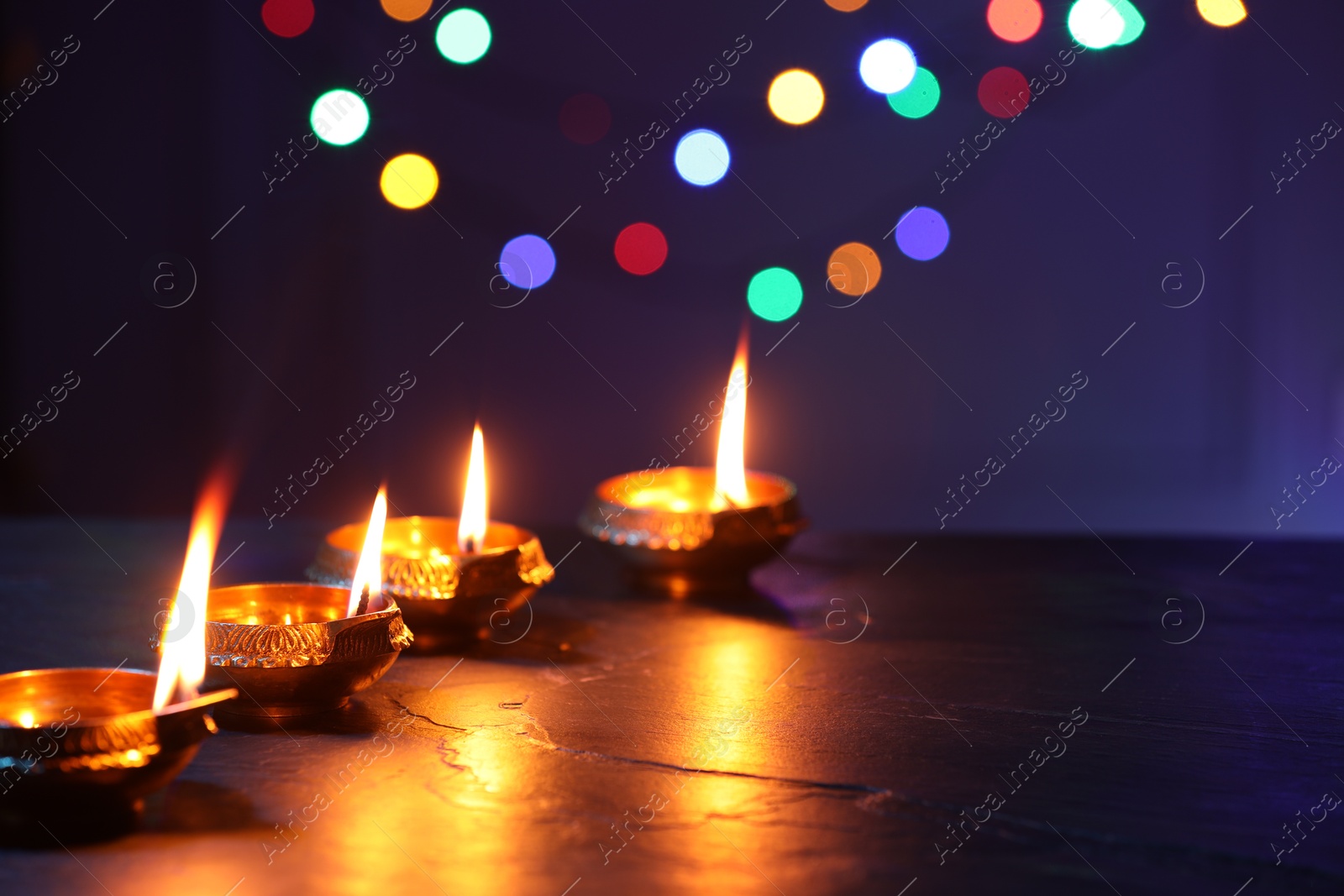 Photo of Diwali celebration. Diya lamps on dark table against blurred lights