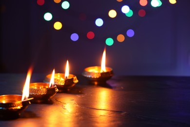 Photo of Diwali celebration. Diya lamps on dark table against blurred lights