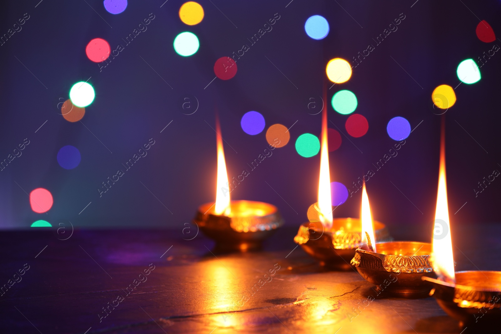 Photo of Diwali celebration. Diya lamps on dark table against blurred lights