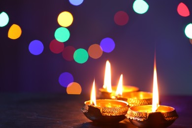 Photo of Diwali celebration. Diya lamps on dark table against blurred lights