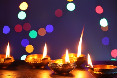 Photo of Diwali celebration. Diya lamps on dark table against blurred lights