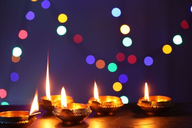 Photo of Diwali celebration. Diya lamps on dark table against blurred lights