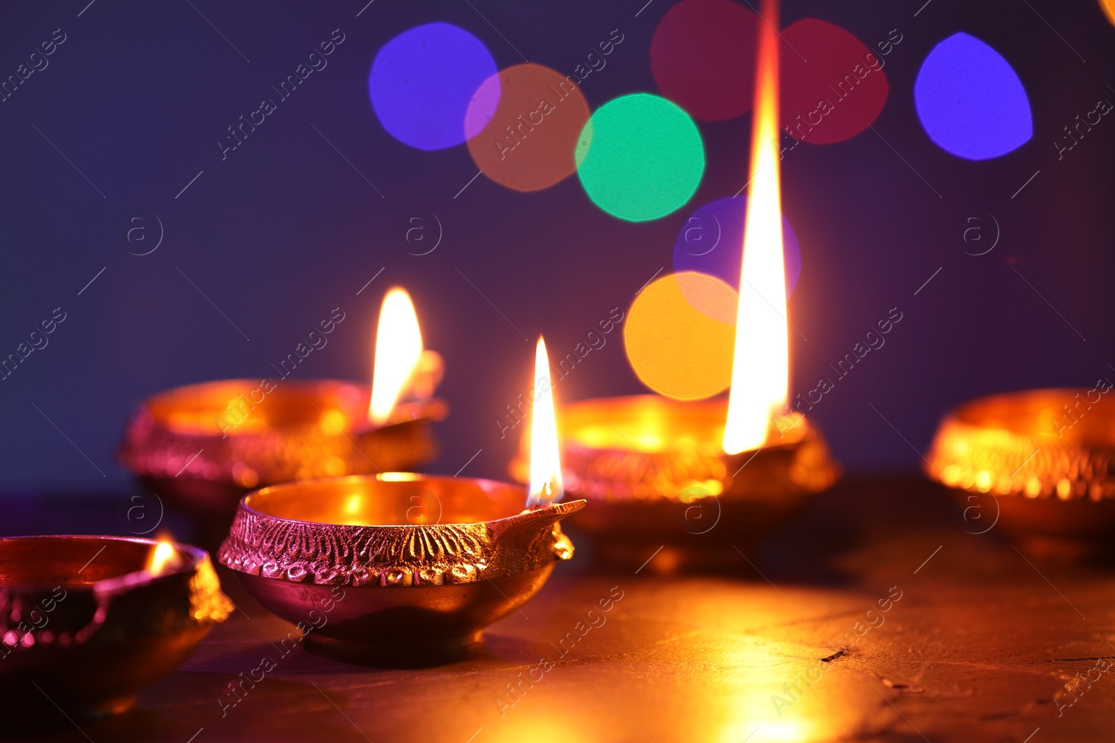 Photo of Diwali celebration. Diya lamps on dark table against blurred lights, closeup