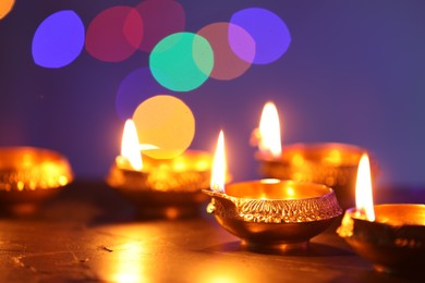 Diwali celebration. Diya lamps on dark table against blurred lights, closeup