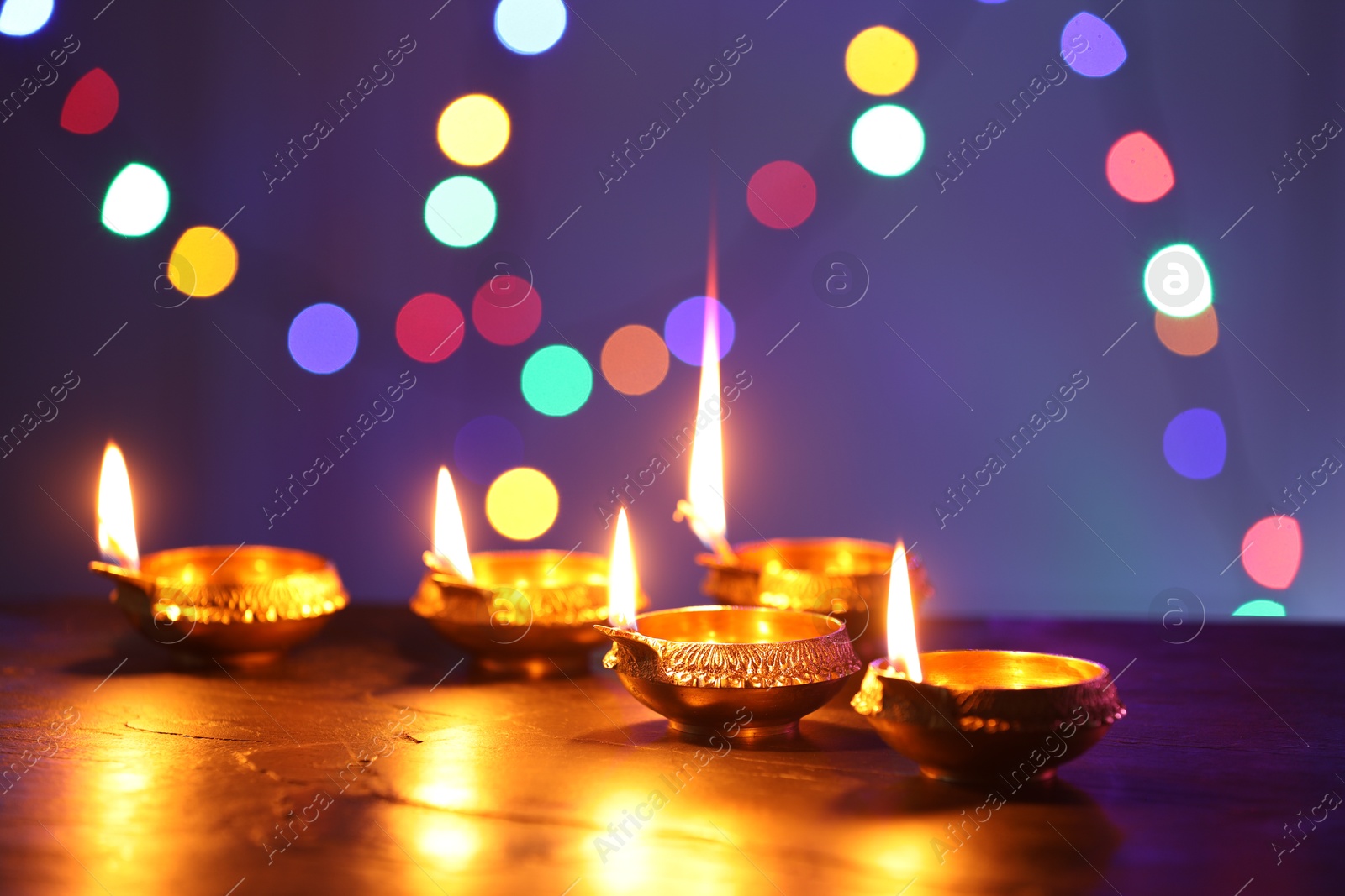 Photo of Diwali celebration. Diya lamps on dark table against blurred lights